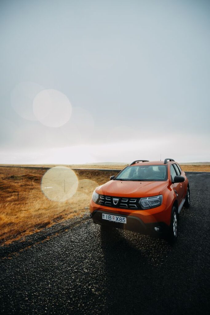 Orange Dacia Duster SUV on a wet rural road under a cloudy sky.