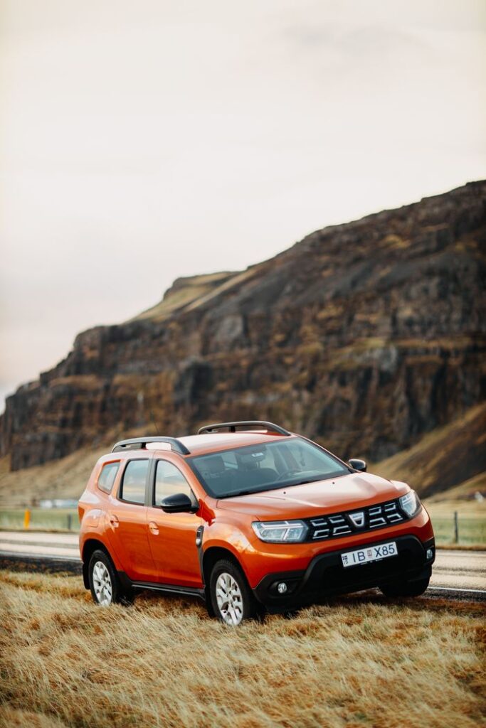 Bright orange SUV on a rural road against a rocky mountain backdrop, perfect for adventure travel themes.