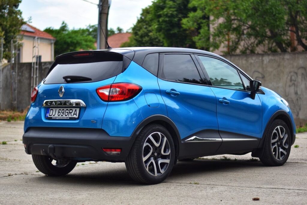 Blue Renault Captur in a parking lot with lush green surroundings.